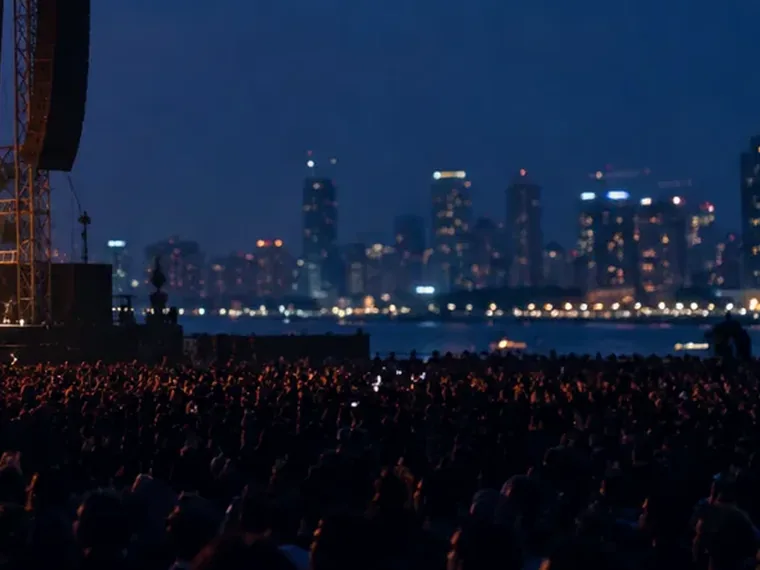A packed open-air crowd with a lit skyline behind